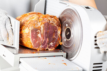 Close up isolated image showing a butcher or chef slicing a large frozen cured meat block. Turkish pastirma, pastrami, ham, beef concept. The person wears protective cut resistant gloves