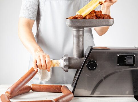 a woman cook wearing apron is stuffing homemade sucuk or sausage into casing using an electrical meat grinder and stuffer. This is an healthier preservative free alternative for these delicious food.