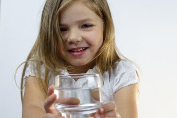 Portrait of a smiling little girl offering a glass of pure water.