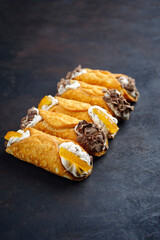 Traditional Italian Sicilian pastry dessert cannoli with creamy ricotta filling, chocolate crisps and glazed lemon slice served as close-up on a rustic black board with copy space