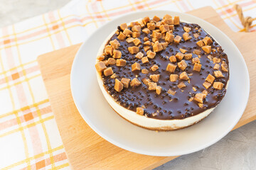 Cheesecake with chocolate frosting and salted caramel pieces on light rustic background. Homemade dessert for birthday, festive party, engagement or Valentine day, selective focus, copy space