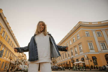 Stylish happy young fair-skinned woman with tousled hair smiles with teeth on city background....