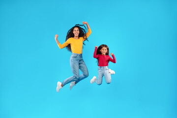 Fototapeta na wymiar Arabic Mother And Daughter Jumping Posing In Mid-Air, Blue Background