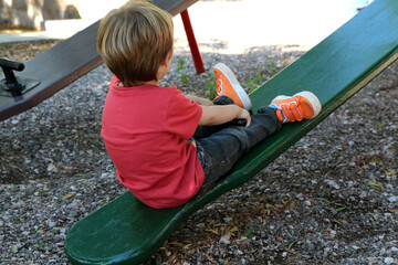 
Little boy playing in the park. Child on a seesaw. Blond boy having fun outdoors on a playground....