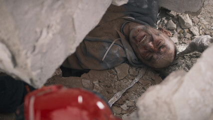 From above aged man suffering from pain and talking with rescuer while lying under concrete rubble...