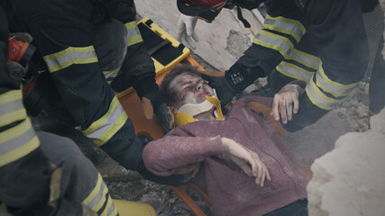 From above men in uniform saving injured teenager from rubble during rescue mission on ruins of...