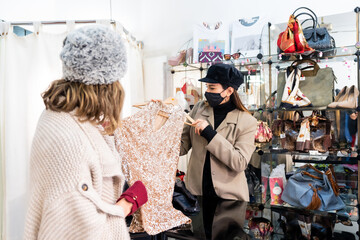 Caucasian employee with a mask from a luxury clothing store testing and showing clothes to a client, security measures in the coronavirus pandemic, covid-19