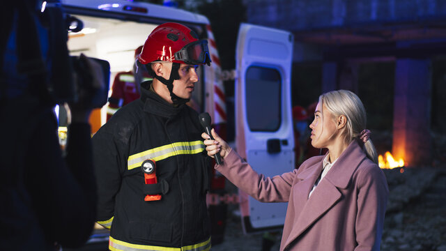 Male emergency service worker speaking while giving interview to female reporter and cameraman near ambulance car and paramedics after disaster