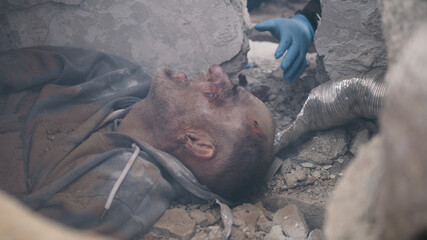 Tilt up view of injured man lying under rubble and talking with emergency service worker during...