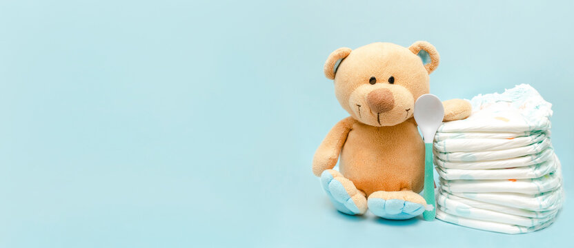 Stack of diapers with cute teddy bear toy on table. set for infant boy girl for baby shower present gift on blue background with copy space. Healthcare medical, hygiene concept
