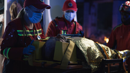 Woman in mask and paramedic uniform talking and supporting injured man near emergency van in evening