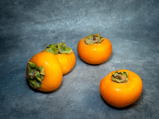 Four persimmons on a black background. Persimmon varieties Chamomile.   Big ripe tasty fruits on the table.