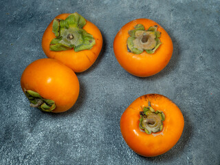 Four persimmons on a black background. Persimmon varieties Chamomile.  Big ripe tasty fruits on the table. View from above