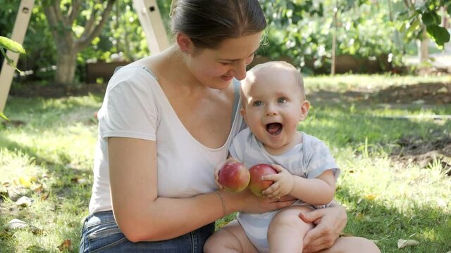 Young mother hugging her baby son aeting ripe apples picked in house backyard garden. Concept of child development, parenting and healthy organic food growing.