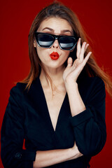 cheerful fashionable woman wearing sunglasses red lips posing red background