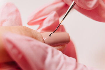 Manicure process. A master manicurist makes a drawing on artificial nails using black varnish and a thin brush.