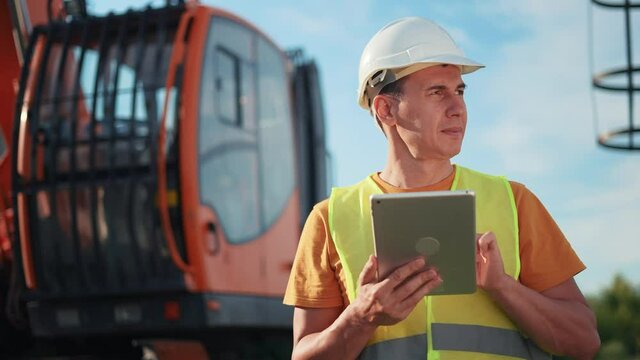 worker in hard a hat with digital tablet near excavator. construction site driver with online digital tablet. industry construction business concept. worker hard hat near excavator truck in uniform.