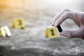 Forensic officer is holding handgun casings or pistol bullet which is important physical evidence while collecting evidence at the scene of the crime. Soft and selective focus. - Powered by Adobe