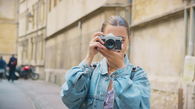 Young woman taking and reviewing picture in city street on retro style digital camera - shot in slow motion