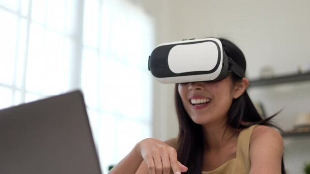 Young asian woman put on vr glasses into virtual simulated world metaverse chatting conference online sitting in living room at home. Business Woman Meeting on social media Learning from home.