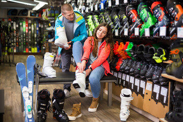 Fototapeta na wymiar Positive couple choosing ski boots for girl in sport goods store