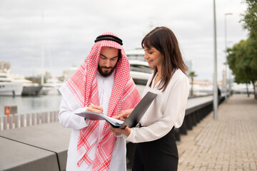 Arab man singing charter contract in order to book yacht while standing in port with businesswoman