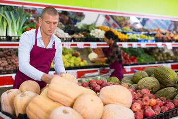 Focused salesman arranging organic fruits and vegetables on shelves at farmers market