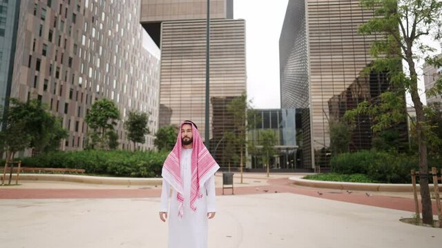 Confident handsome arab man in traditional saudi clothes standing alone at empty square outdoors