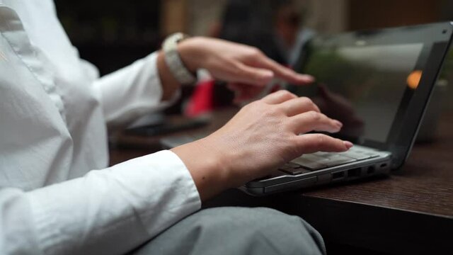 Close up on hands of unknown caucasian woman sitting at the table at cafe or restaurant working on the computer laptop typing 
