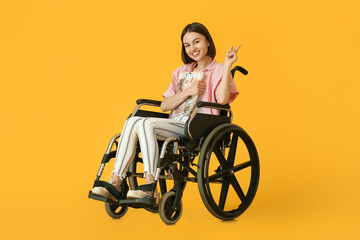 Young woman in wheelchair and with magazine on color background