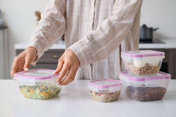 Woman packing meal into lunch box on table in kitchen