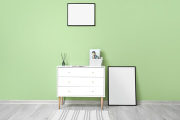 Blank frames and chest of drawers with reed diffuser near green wall