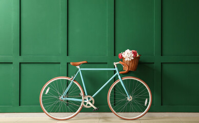 Stylish bicycle with wicker basket and flowers near green wall