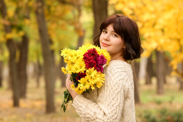 Naklejka premium Pretty woman with bouquet of beautiful chrysanthemum flowers in autumn park