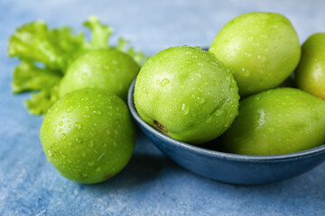 Bowl of green tomatoes with water drops on color background, closeup