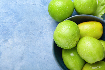Bowl of green tomatoes with water drops on color background, closeup