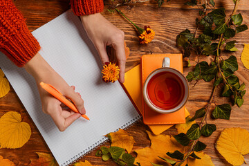 Woman with flower writing in notebook on wooden background