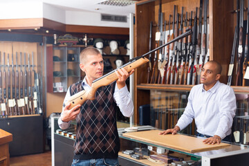 Portrait of interested man carefully choosing hunting break barrel rifle in modern gun shop