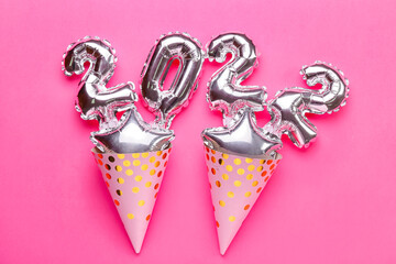 Composition with figure 2022 made of silver balloons and party cone hats on color background