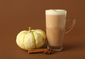 Glass cup of tasty pumpkin latte on brown background