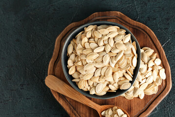 Bowl and spoon with natural pumpkin seeds on black background