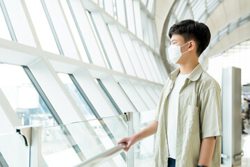 Young and handsome Asian teenager boy with medical face mask standing alone at the airport terminal waiting for boarding. Travel, Restriction, Covid 19, Pandemic, Protection, New normal, Copy space
