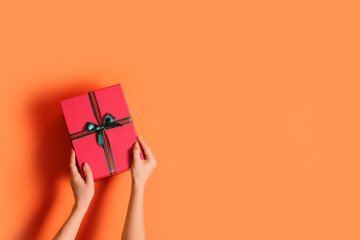 Female hands with beautiful Christmas gift box on orange background