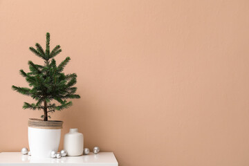 Beautiful Christmas tree in pot with balls on table near beige wall