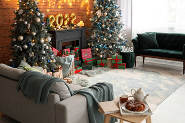 Interior of festive living room with Christmas trees, decorative mantelpiece and sofas