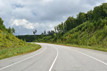 Turn of the road. Hills on both sides of the roadway. Summer time, cloudy sky.