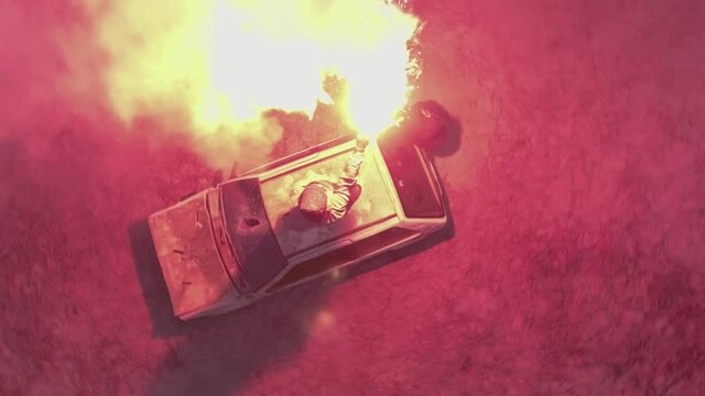 Riot man with flare grenade smoke football hooligan stands on car hood spinning smoking burning warm trashed wrecked war zone dramatic drama fight broken red fiery burn lit fire beach bright lights