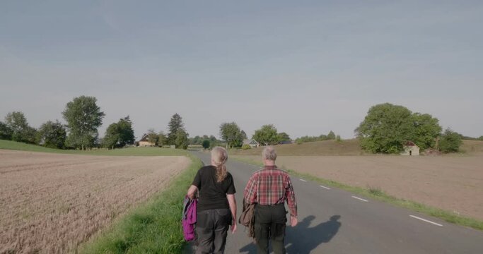 Elderly Couple Walks Together On a Countryside Road in Late Summer, High angle Medium Shot Tracking Forward