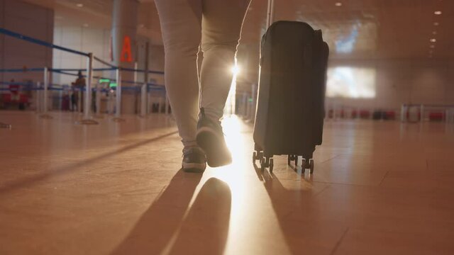 Close up view of a tourist woman pulling a carry on suitcase at the airport terminal. Travel concept, slow motion. 