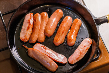 half-cut sausages are fried in oil in a black cast iron skillet